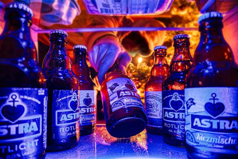 Beer bottles inside a fridge, and a human man getting one. Let's see how long to chill beer in fridge, and tips to speed up the process.
