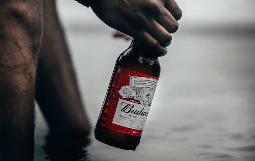 a man's hand pulling a bottle of beer out of the river